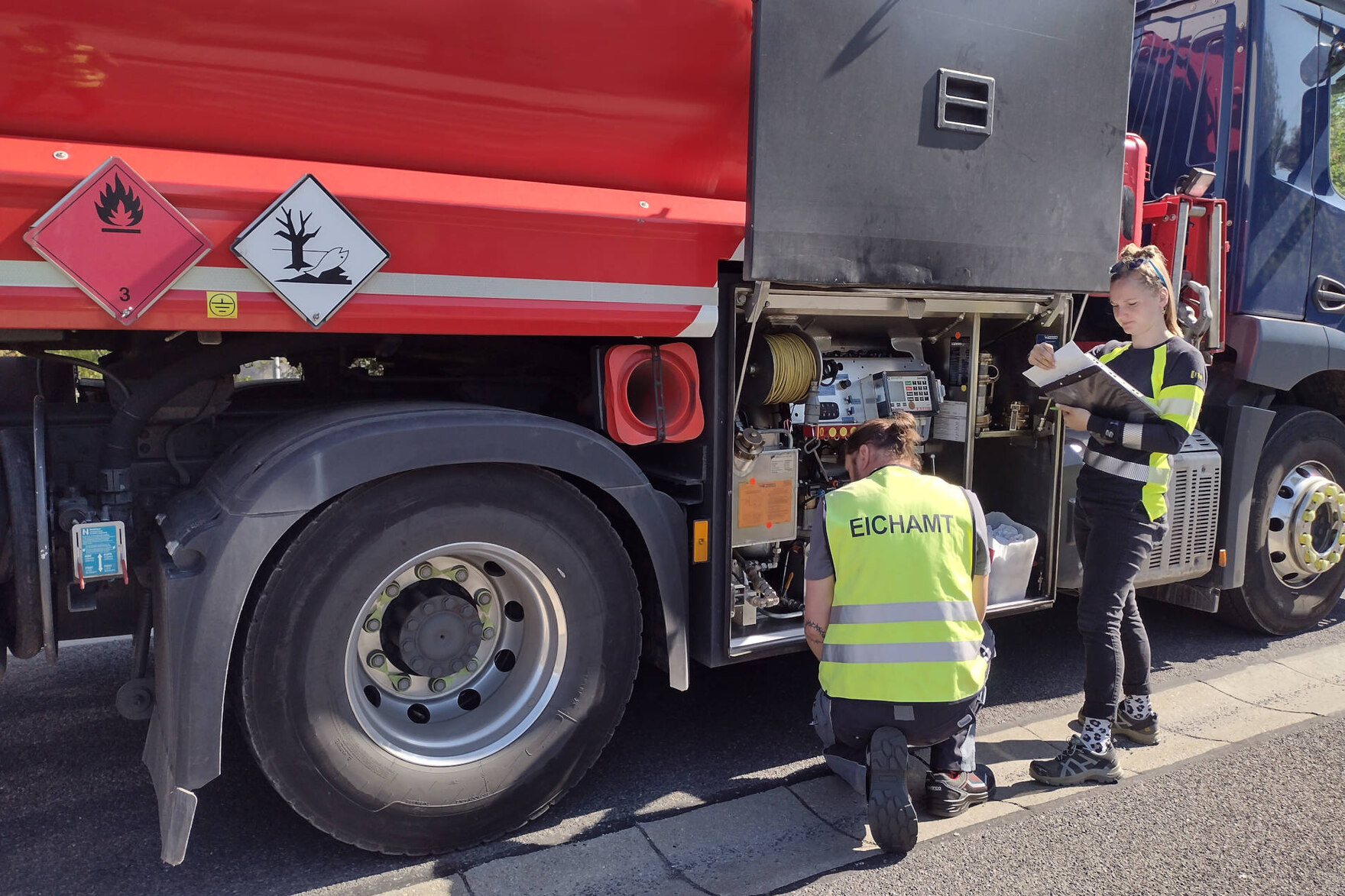 Überprüfung eines Tankwagens: Zwei Bedienstete des Eichamts stehen vor der Messanlage und kontrollieren deren Gesetzeskonformität